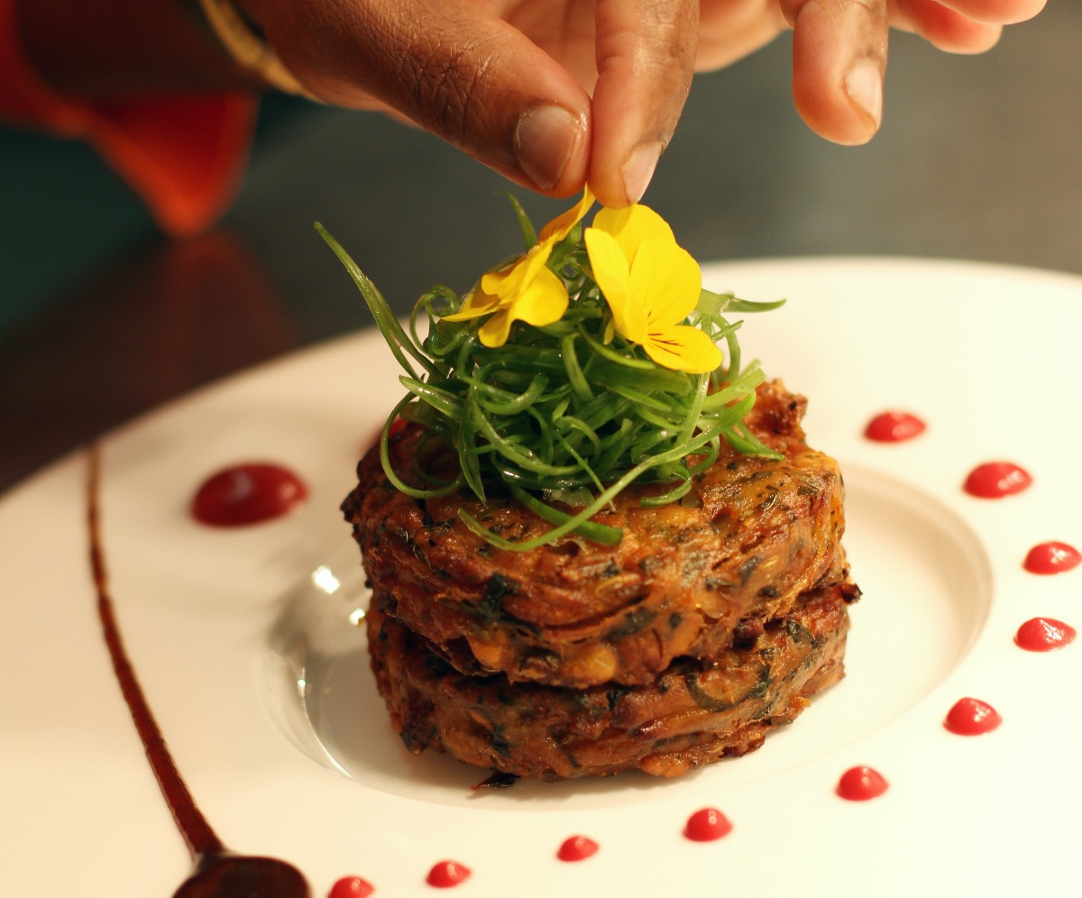 Two pakoras piled on a plate with shredded spring onion and topped with yellow flowers